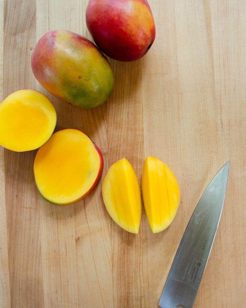 Mango in various stages of how to cut a mango on a cutting board with a knife.