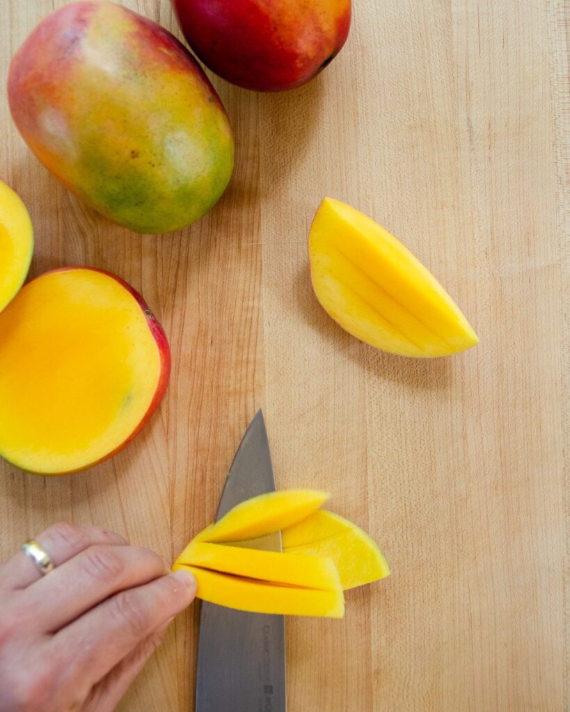 A knife cutting the slices of mango off the peel.