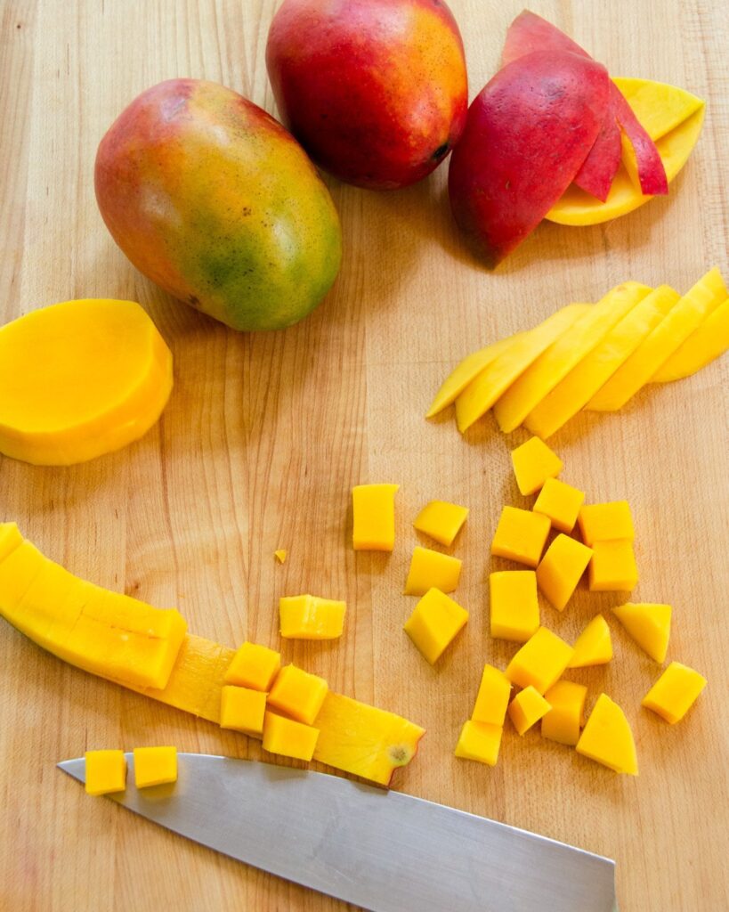 Whole mangos on a cutting board with a cut up mango and a knife.
