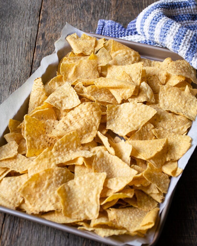 Corn tortilla chips on a baking sheet with a striped blue towel.