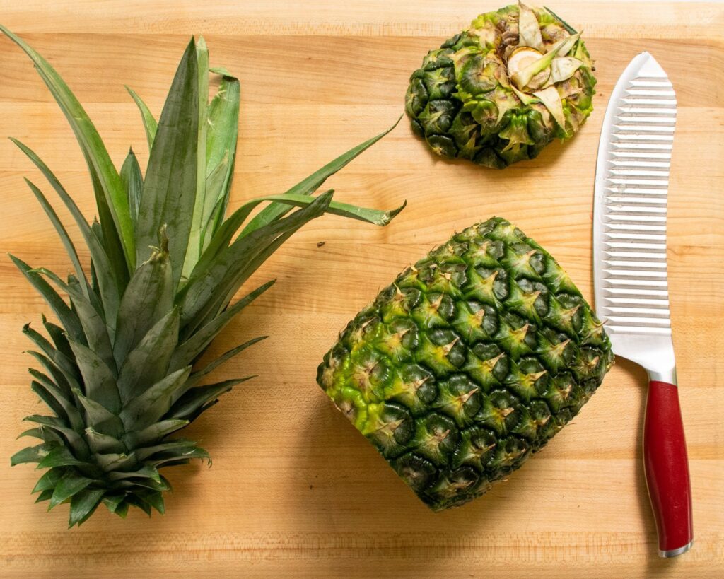 A pineapple with the leaves and both ends sliced off on a cutting board.