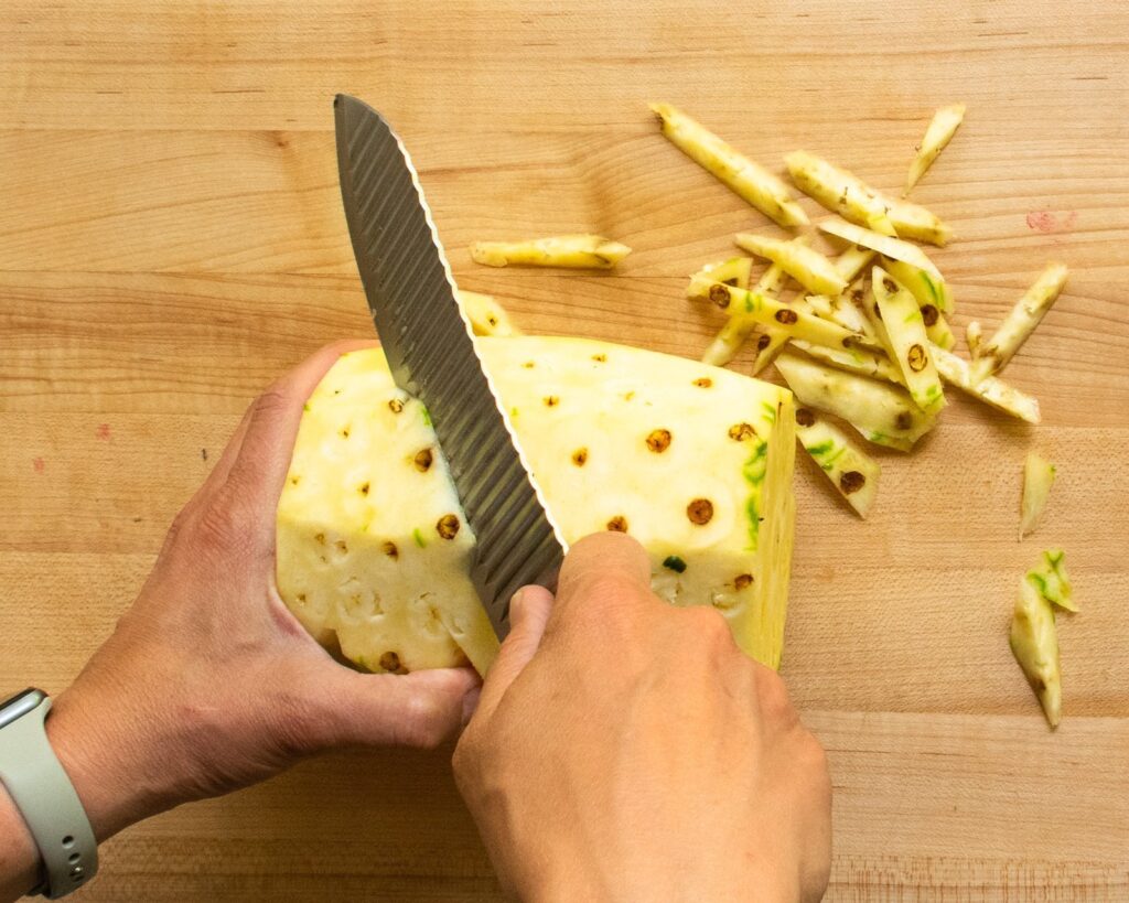 Two hands slicing the "eyes" out of the pineapple.