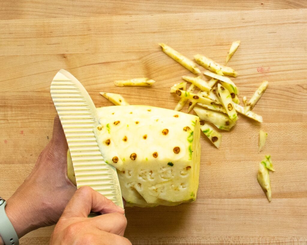 Two hands removing the "eyes" of a pineapple - one stage in how to cut a pineapple.