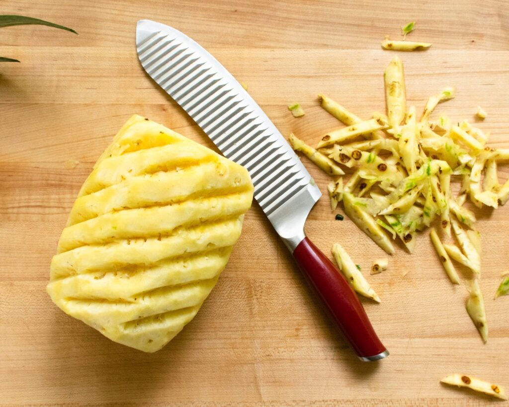 A pineapple with all the "eyes" removed on a wooden cutting board.