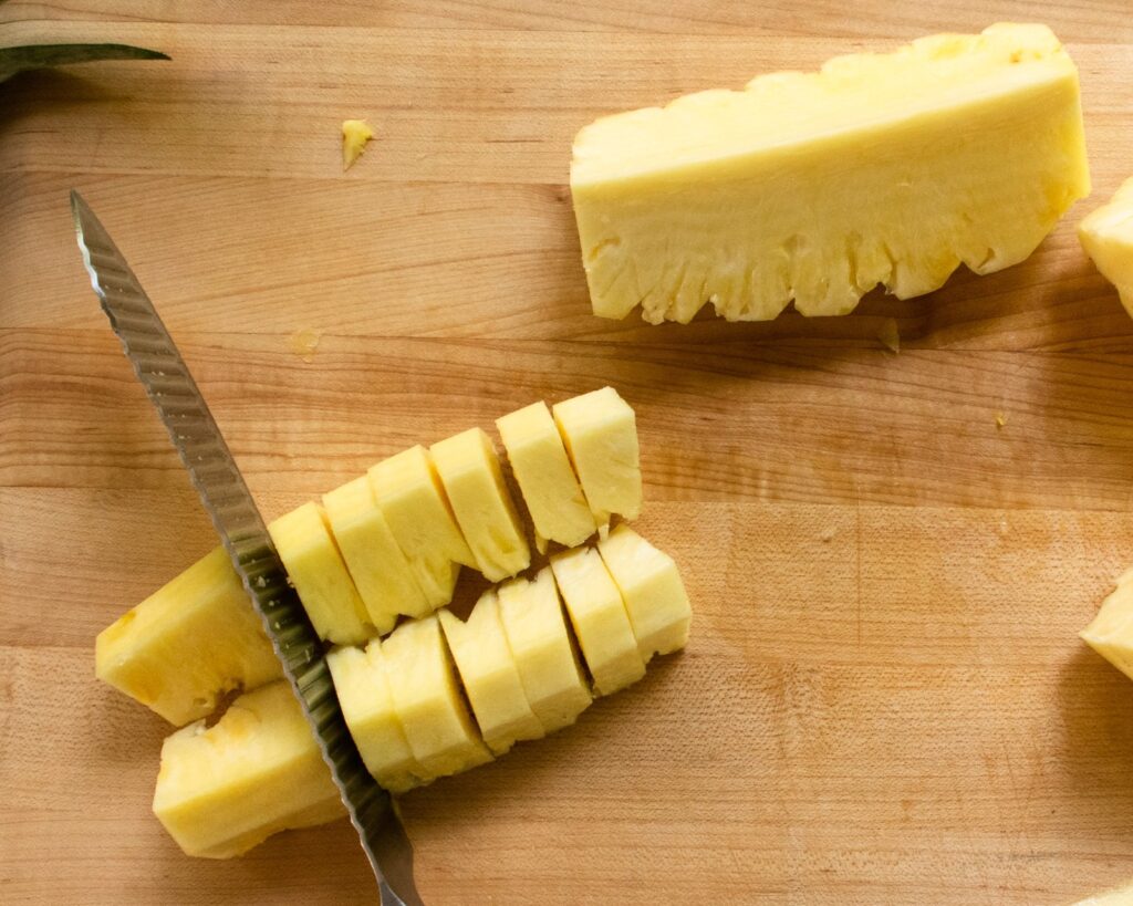 A knife slicing pineapple into pieces.