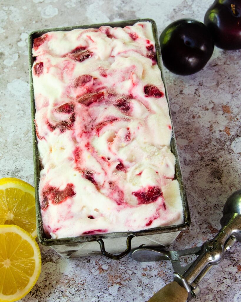 A loaf pan with plum lemon buttermilk ice cream in it. Plums and lemons on the side.