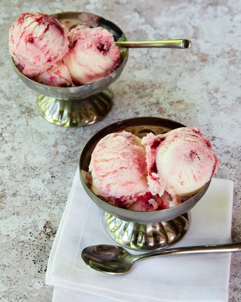 Two small silver dishes with ice cream and teaspoons.