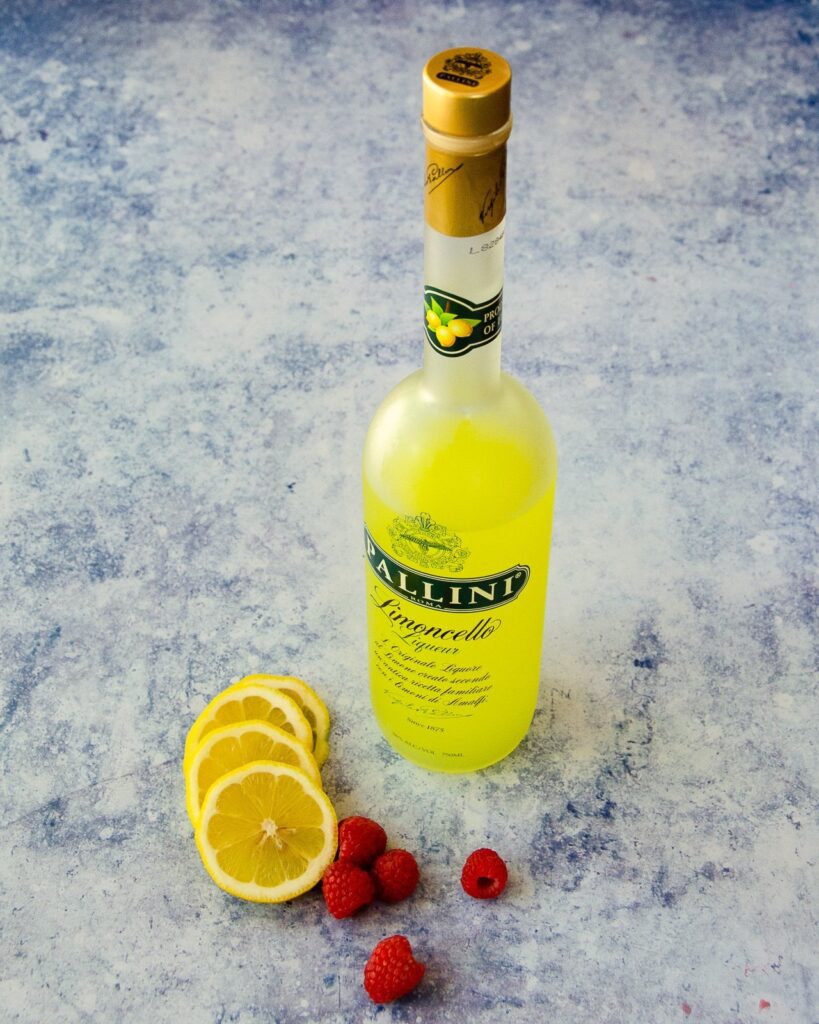 A bottle of limoncello with lemons and raspberries on a counter.