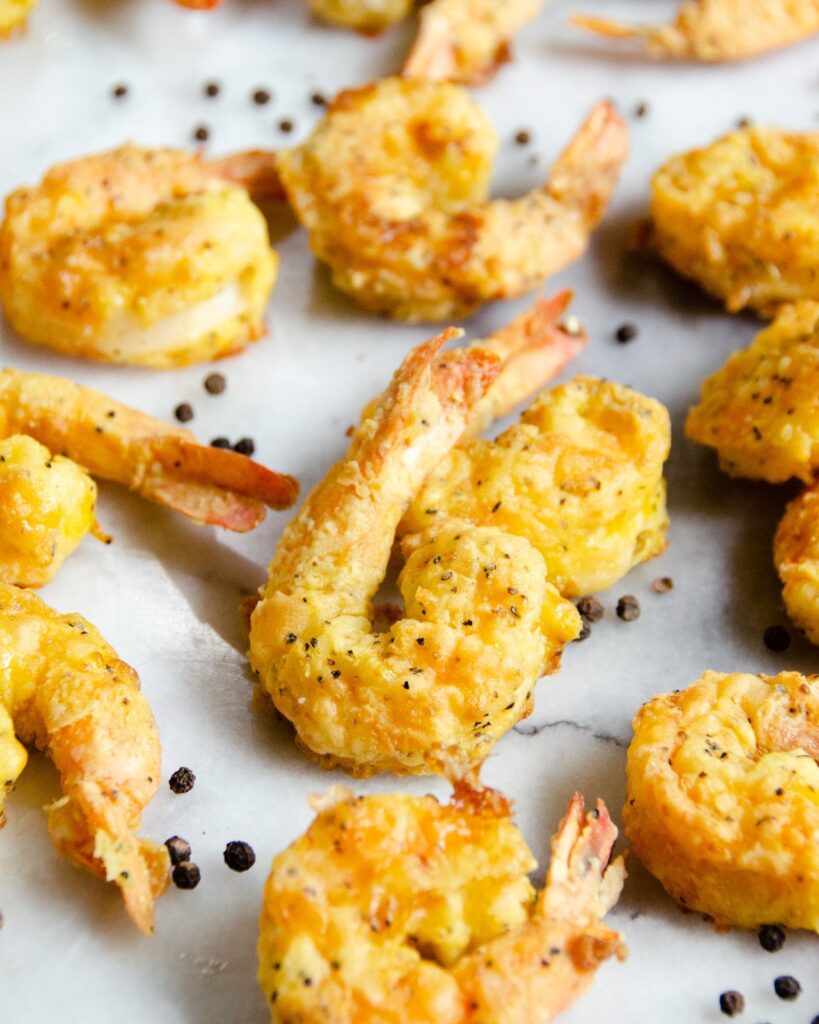 Salt and  pepper shrimp on a marble surface with black peppercorns scattered about.