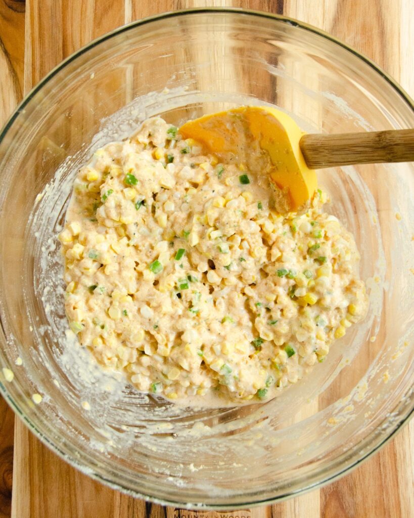 Spicy Corn  Cake batter in a glass bowl with a yellow spatula.