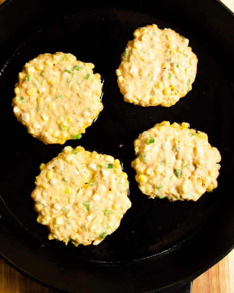 4 corn cakes cooking  in  a cast iron pan.