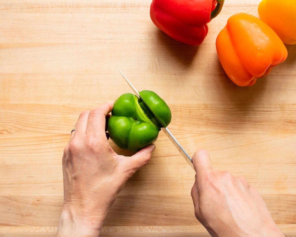 Hands showing how to cut a bell pepper on aa cutting board.