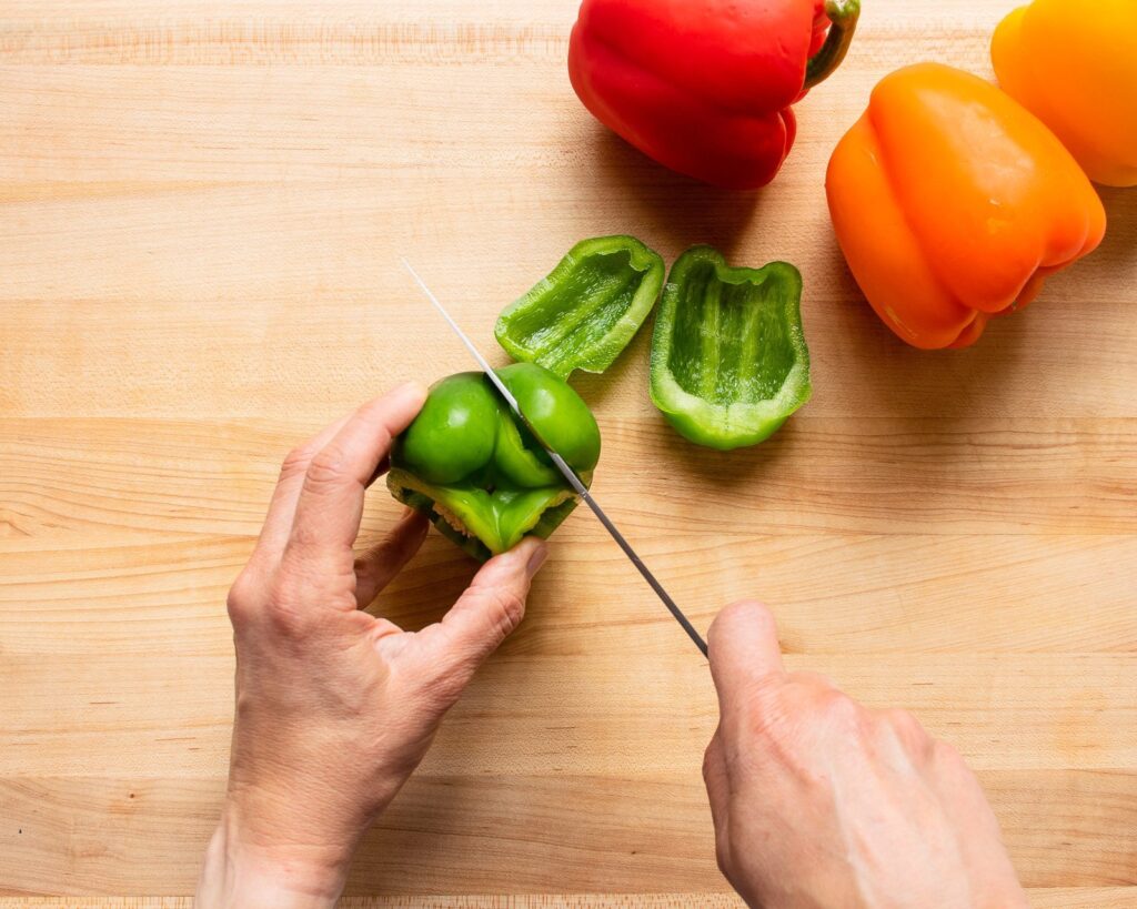 Hands cutting the sides off a bell pepper.