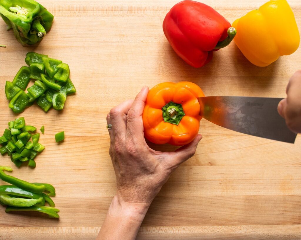 An orange pepper having the top cut off on a cutting board.