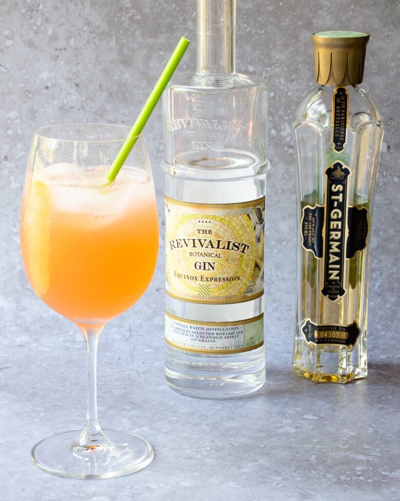 Pamplemousse fizz in a wine glass with a bottle of gin and elderflower liqueur behind it.