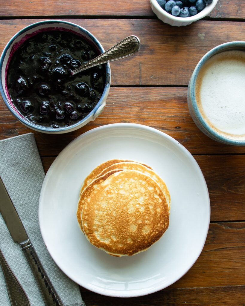 A stack of pancakes on a white plate before compote is put on top.