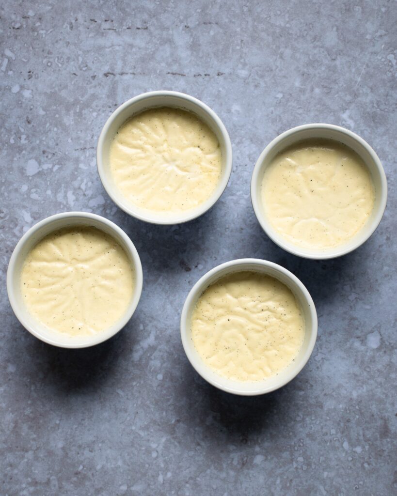 4 white ramekins of panna cotta on a cement counter.