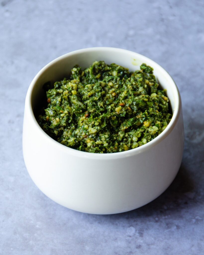 Pesto in a small white dish on a cement countertop.
