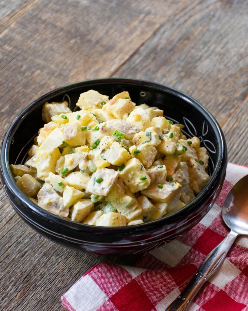Potato Salad in a black bowl on a wooden table.