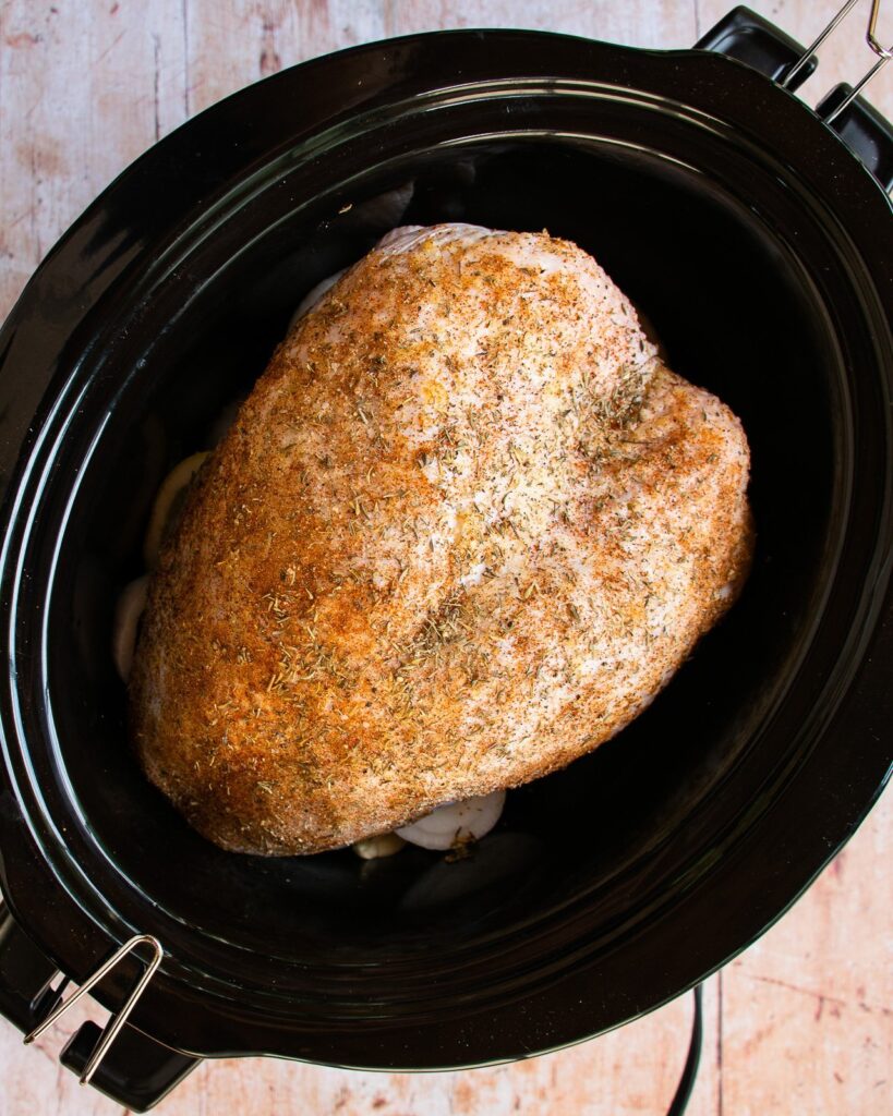 Raw turkey breast with a spice rub in a slow cooker.