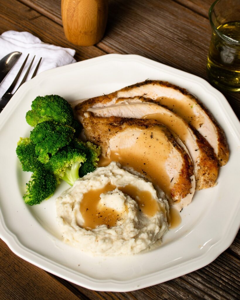 Slices of roast turkey breast on a plate with mashed potatoes and broccoli.