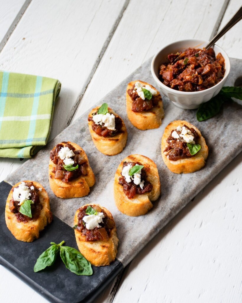 Tomato Jam and goat cheese crostini on a grey platter with green napkins. 