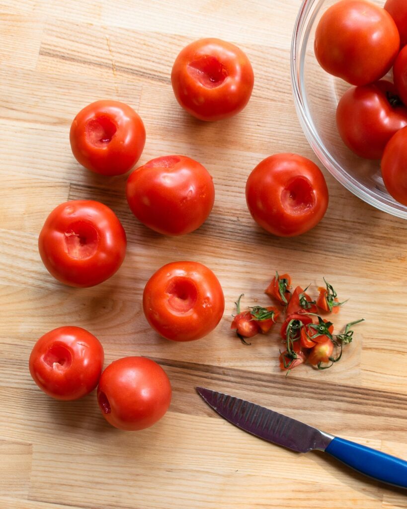 Tomatoes on a cutting board with a paring knife, having been cored - the first step in making tomato concassé