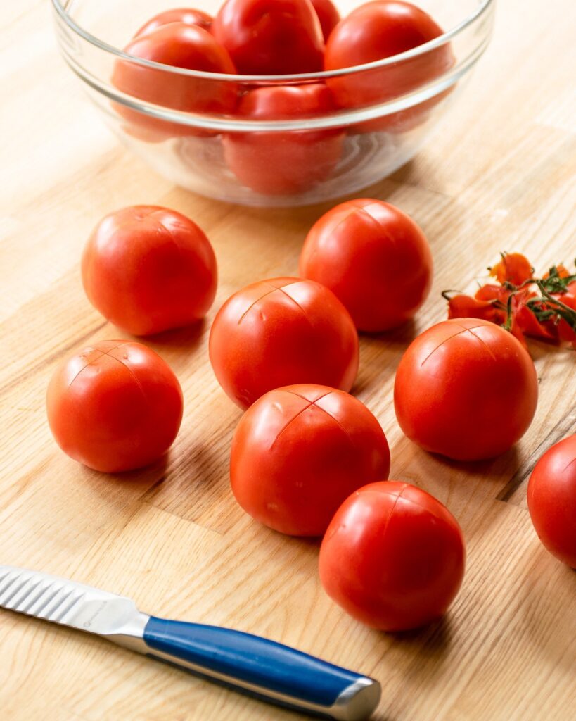 Tomatoes on a wooden cutting board, having been scored.