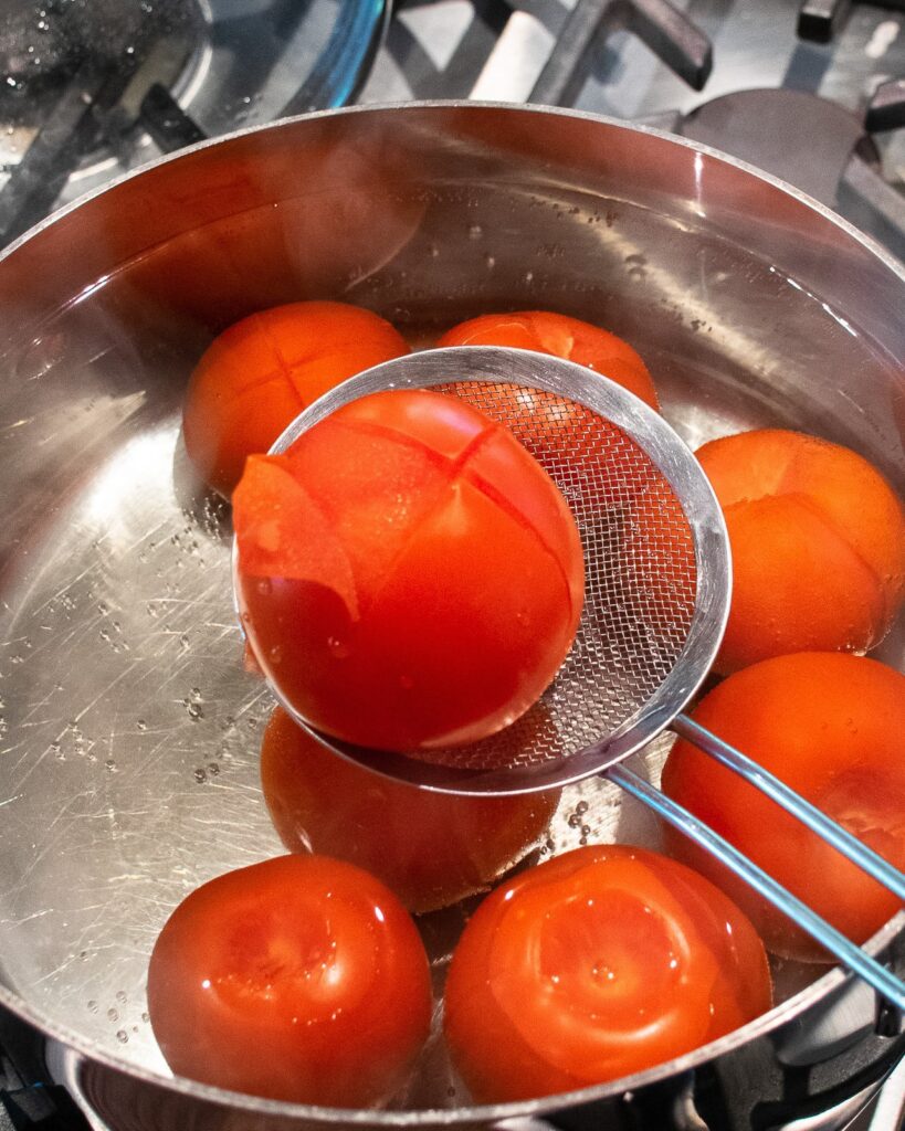 A tomato being pulled out of a stockpot, showing the peel coming off the tomato.