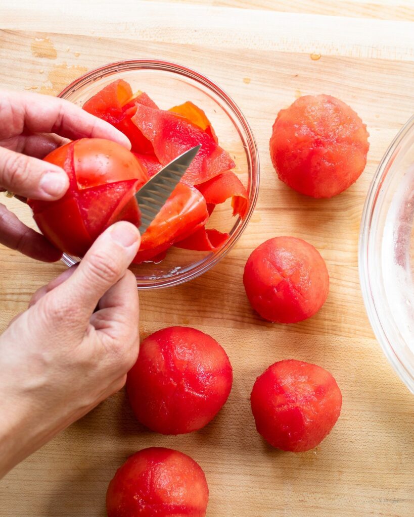 Two hands peeling blanched tomatoes.