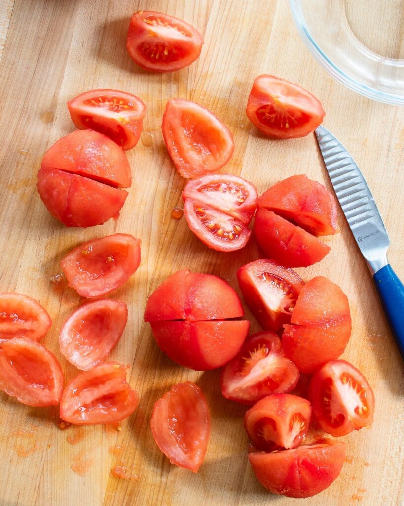 Tomatoes on a cutting board, peeled and in the process of being seeded.