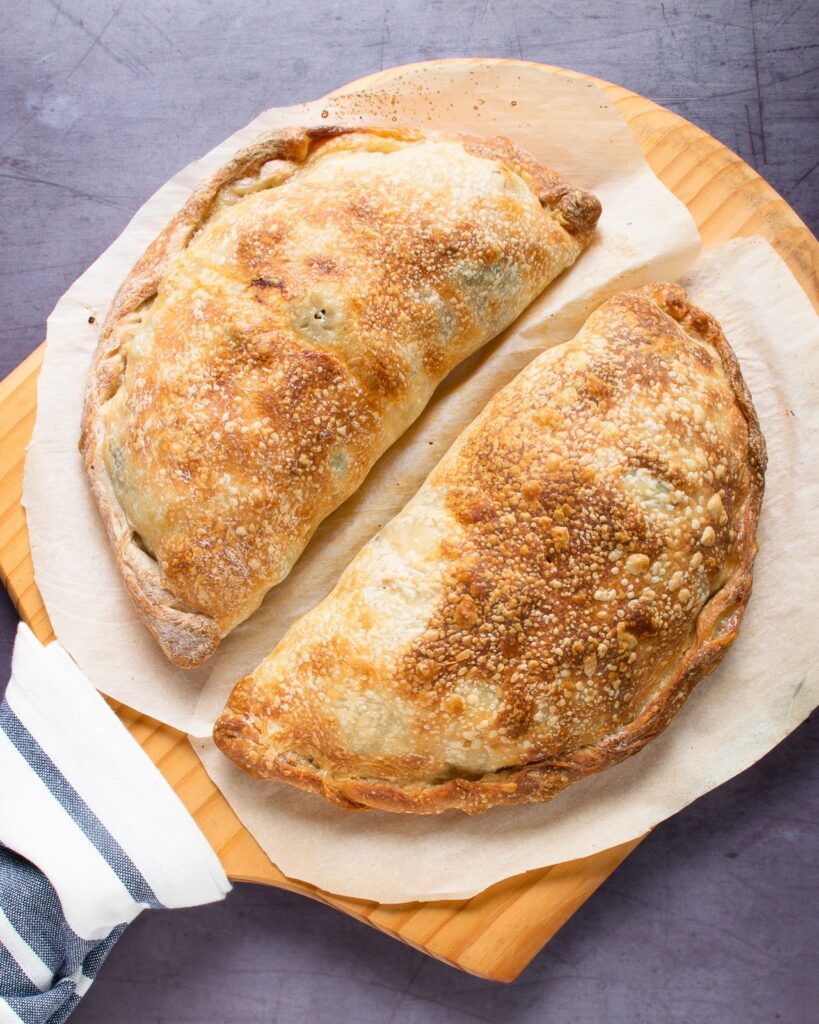 Two baked turkey mushroom broccoli calzone on a pizza peel.