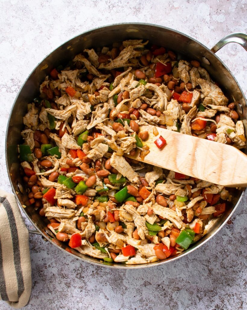 Filling for enchiladas in a saute pan with a wooden spoon.