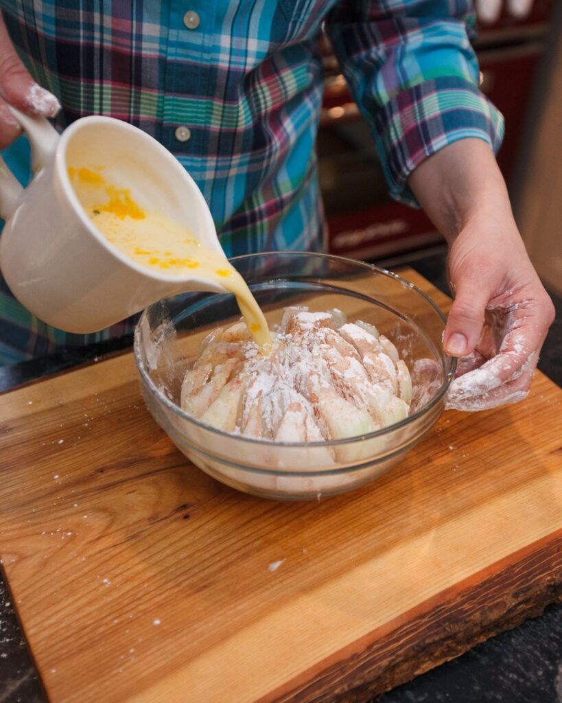 Pouring egg wash over a dredged onion in a bowl.