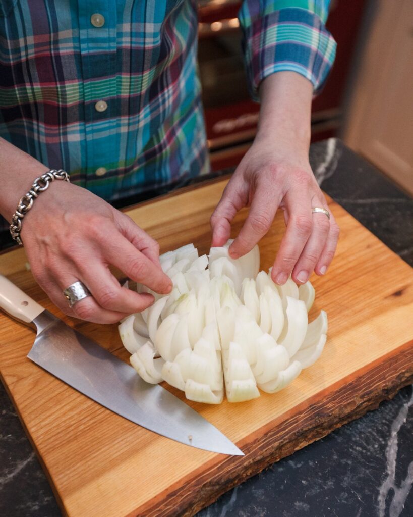 Opening up a sliced onion on a cutting board with a knife near by.