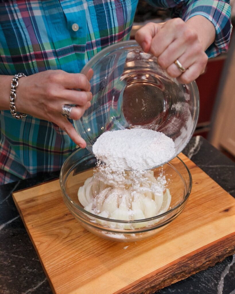 Pouring seasoned flour over an onion in a bowl.