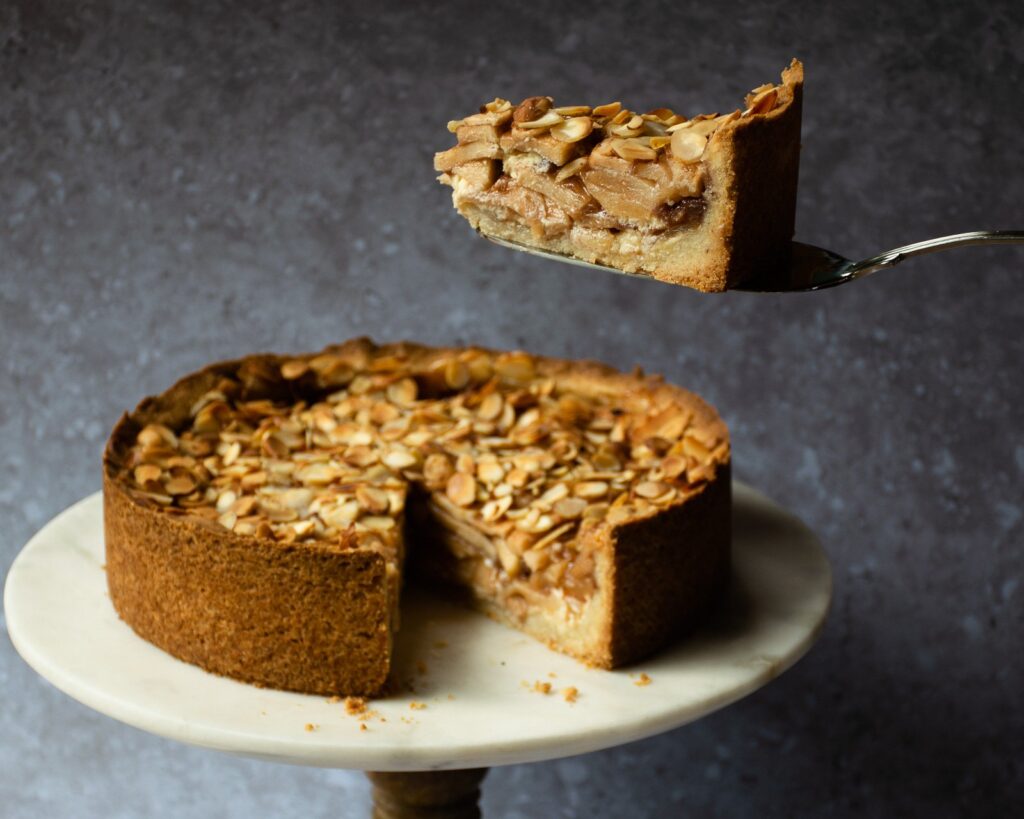 A piece of apple almond torte being lifted out of the torte with a pie server.
