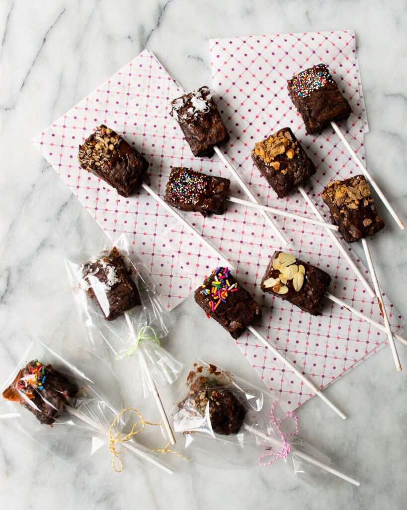 Brownie pops on a marble counter with red polka dot paper and some in cellophane wrappers.