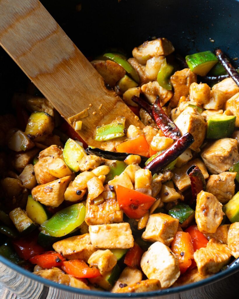 Kung Pao Chicken and Vegetables in a pan with a wooden spoon.