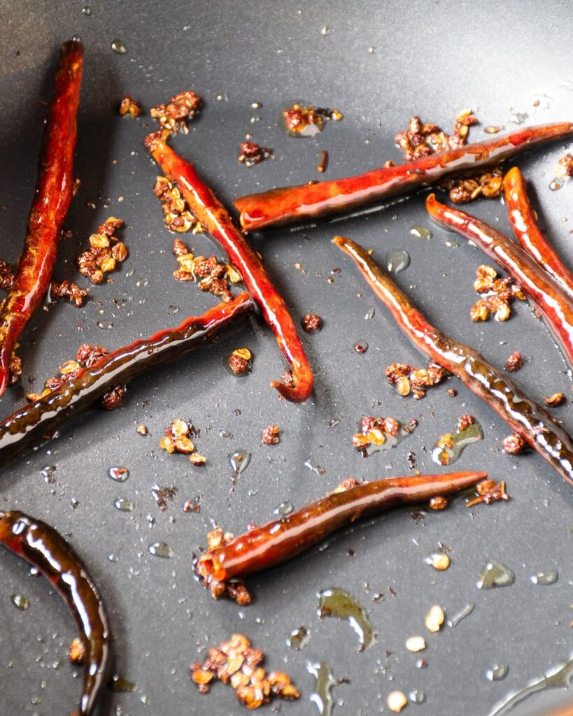Dried red chili peppers and sichuan peppercorns charring and toasting in a pan.