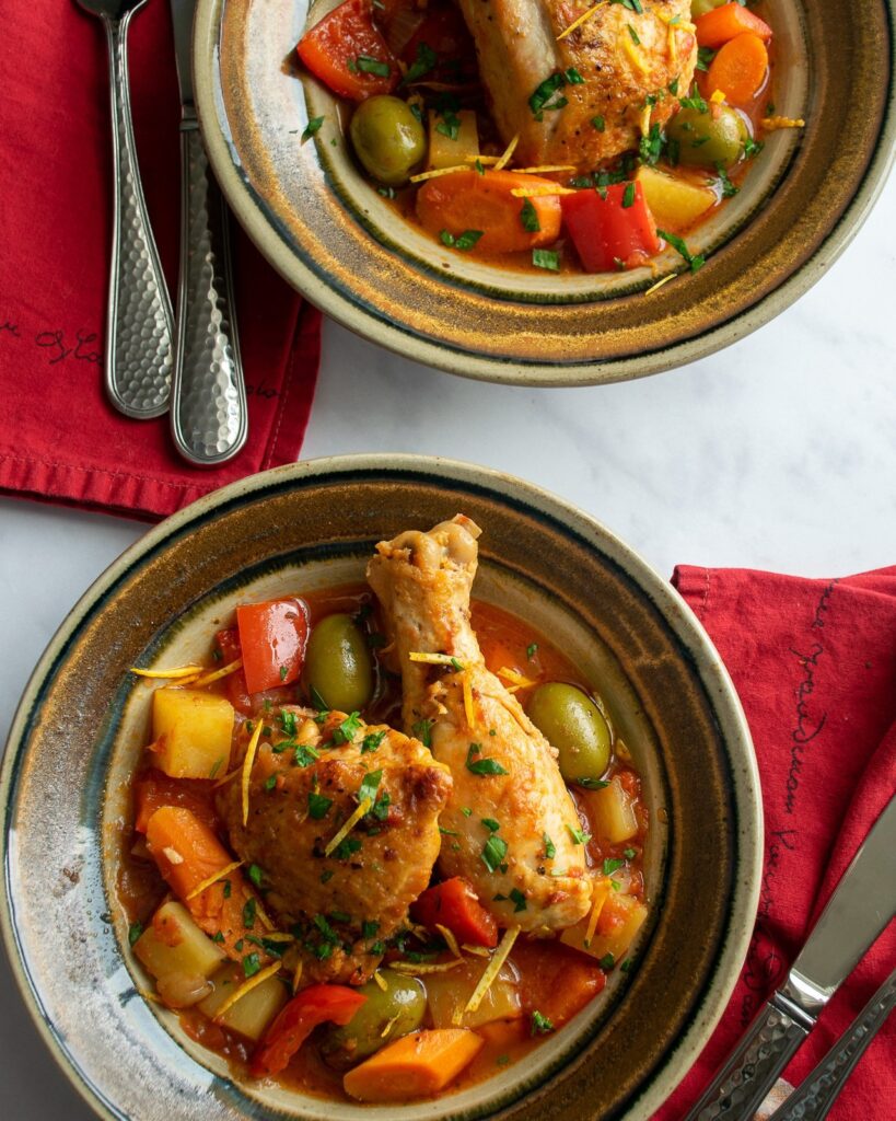 Two brown bowls with Spanish style chicken stew, red napkins, forks and knives.