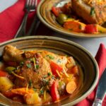 Spanish style chicken stew in two bowls on a marble countertop with red napkins, forks and knives.