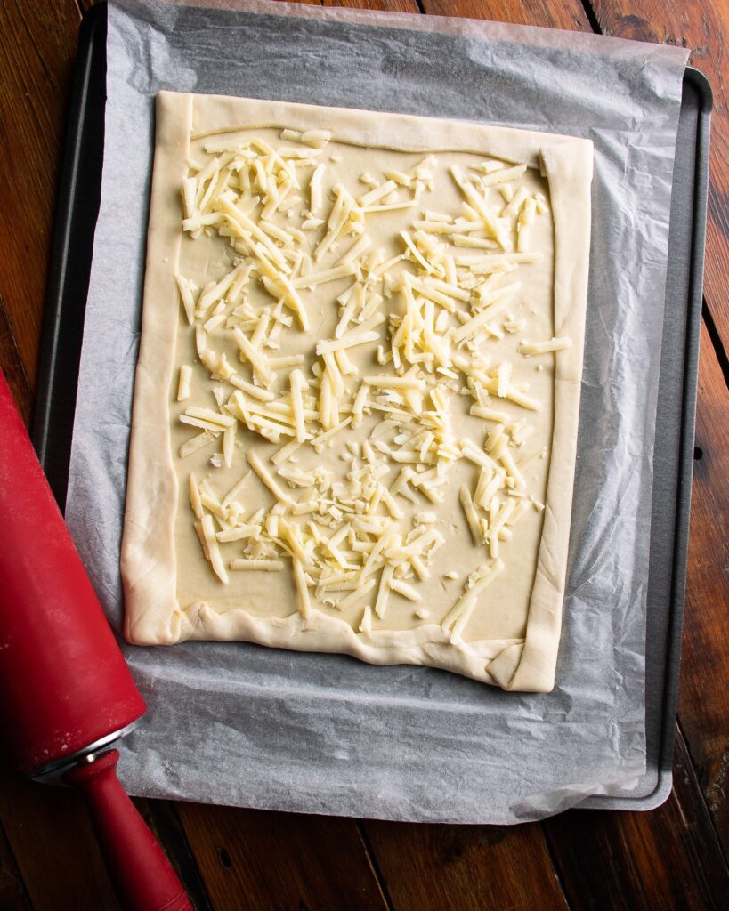 Puff pastry, rolled out on parchment paper on a sheet pan with a red rolling pin.