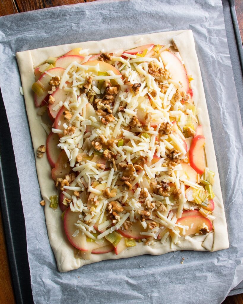 Apple leek cheddar tart ready to go into the oven with walnuts and Cheddar cheese on top.