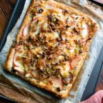 Apple leek cheddar tart, fully baked coming out of the oven on a sheet pan.