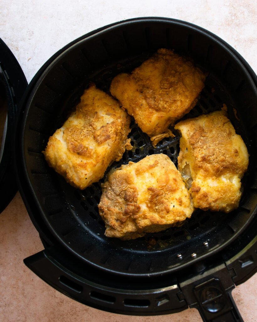 Beer-battered cod in the basket of an air fryer.