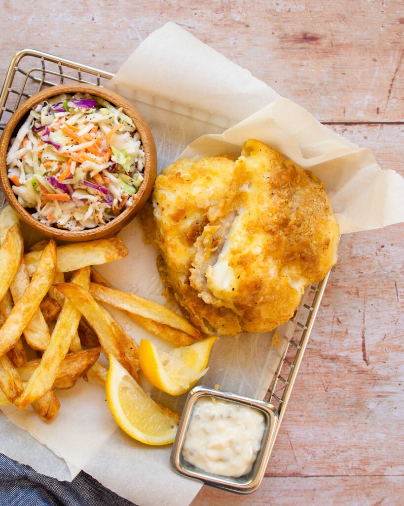 Beer-battered fish and chips in a parchment paper lined basket with a side of coleslaw and tartar sauce.