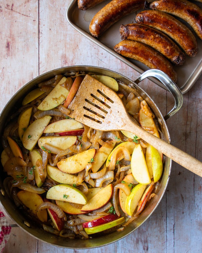 Apples and onions in a sauté pan with a wooden spatula.