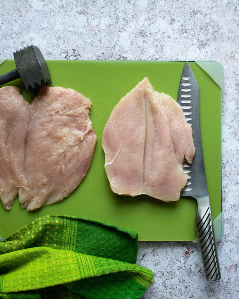 Two butterflied chicken breasts on a green cutting board.