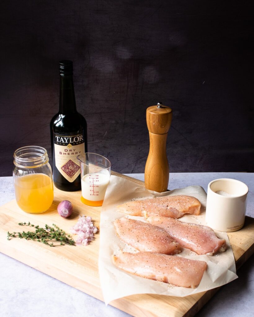 Ingredients on a cutting board - chicken breasts, chicken stock, sherry, cream, thyme, shallots, salt and pepper.